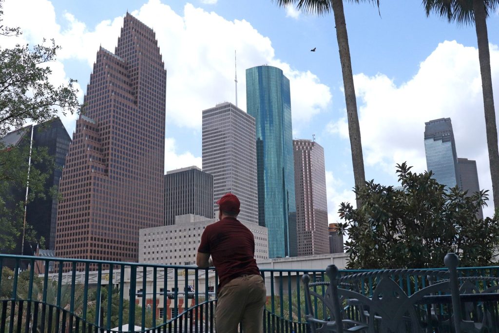 Picture of a person standing in front of skyscrapers in Downtown Houston. The person is facing away from the camera. It is meant to imply careful consideration.